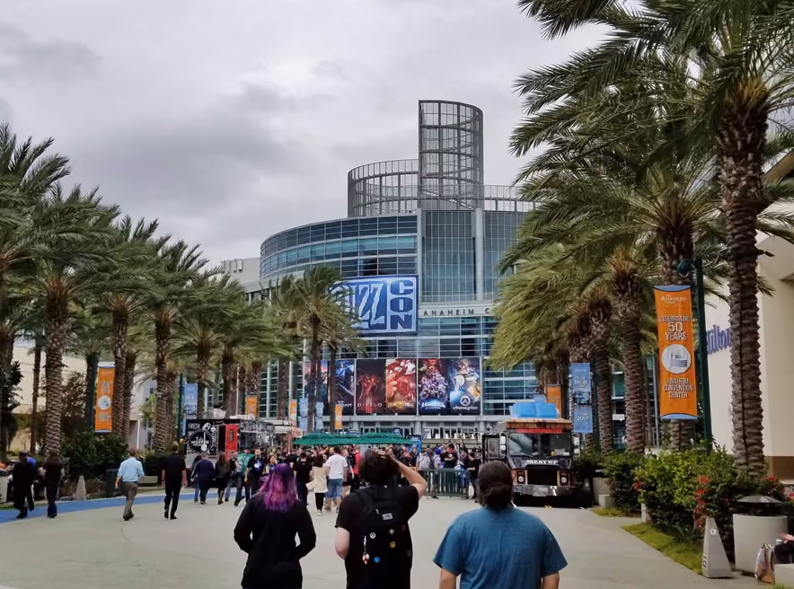 La façade vitrée de l’Anaheim Convention Center un jour de BlizzCon, le logo bleu du salon au-dessus des affiches de Warcraft, Diablo, Hearthstone et Overwatch, des palmiers de chaque côté et des visiteurs en tee-shirt noir qui remontent l’allée.