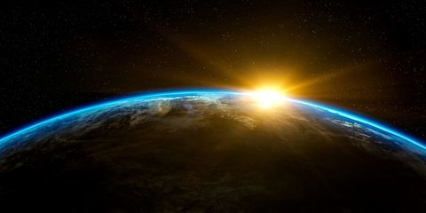 La courbe de la Terre vue de l’espace, un lever de soleil éclatant à l’horizon, l’atmosphère soulignée d’un fin liseré bleu sur un ciel étoilé.