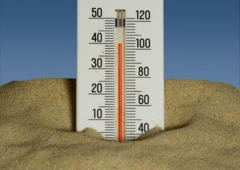 A thermometer stuck in the sand against a blue sky, the mercury climbed toward 40°C.